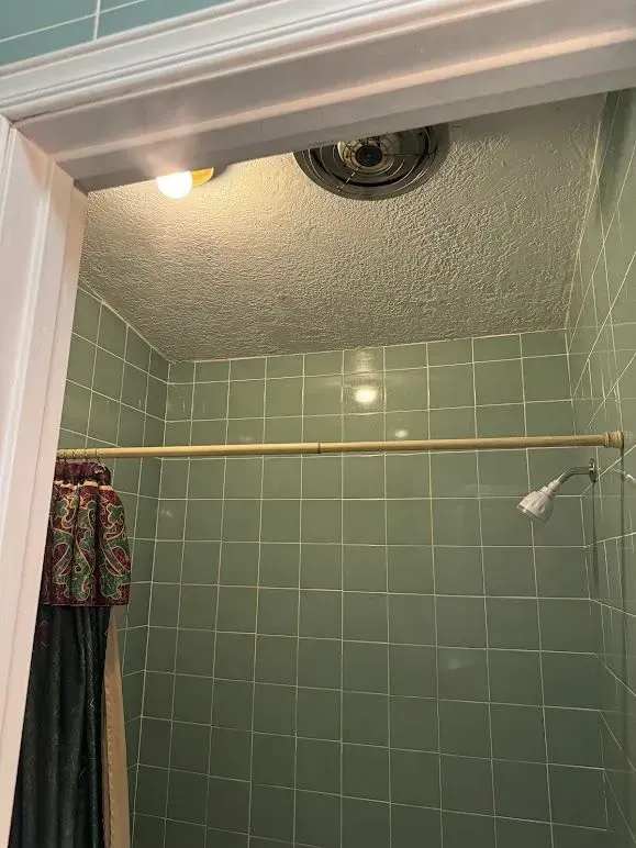 A bathroom with green tiles and a shower curtain.