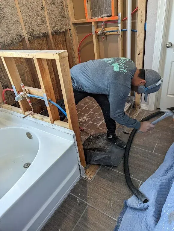 A man is using a vacuum cleaner in a bathroom next to a bathtub.