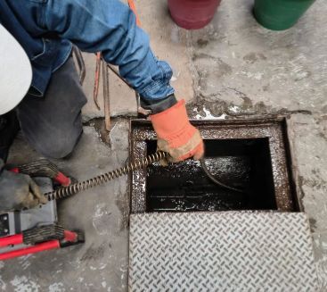 T&eacute;cnico con guantes introduciendo cable en coladera de concreto