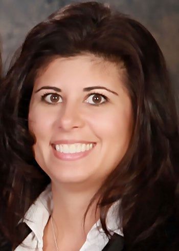 Smiling woman with dark hair in a white collared shirt against a dark background