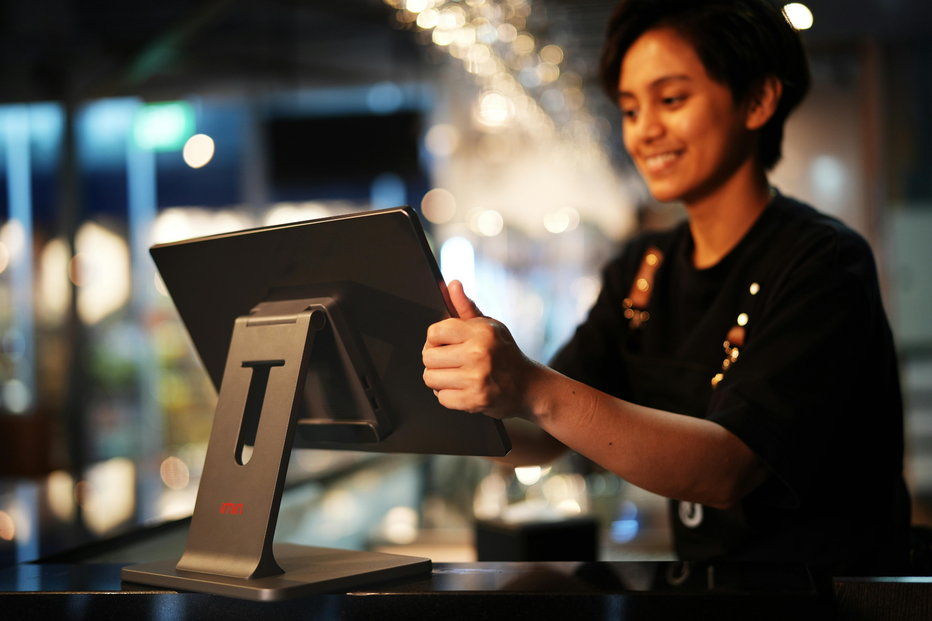 Smiling cashier using a touchscreen register at a softly lit counter