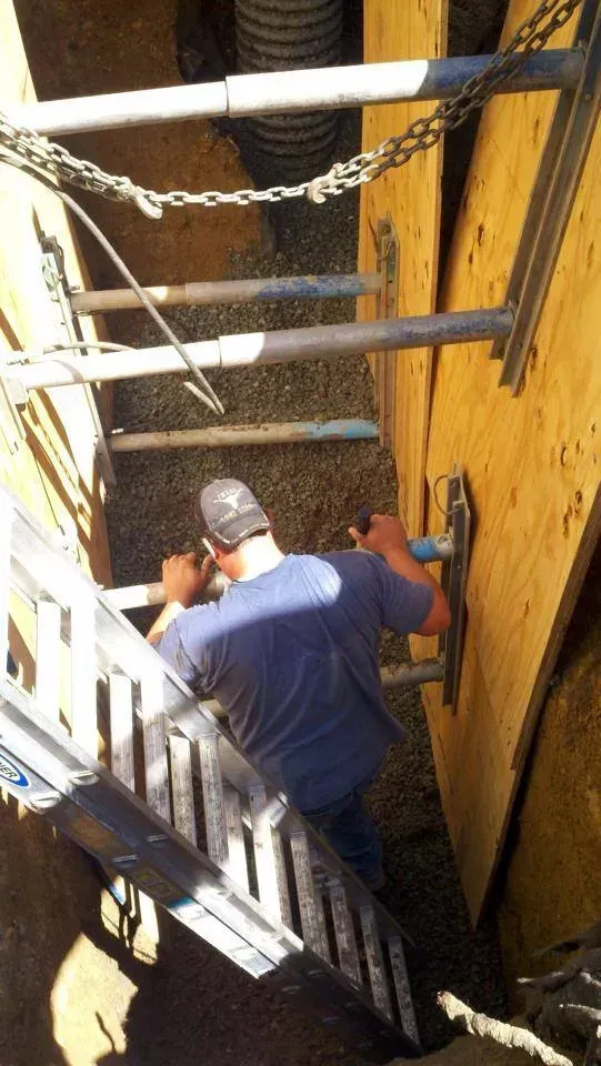 Worker in blue shirt and cap climbing a narrow ladder in a yellow industrial shaft