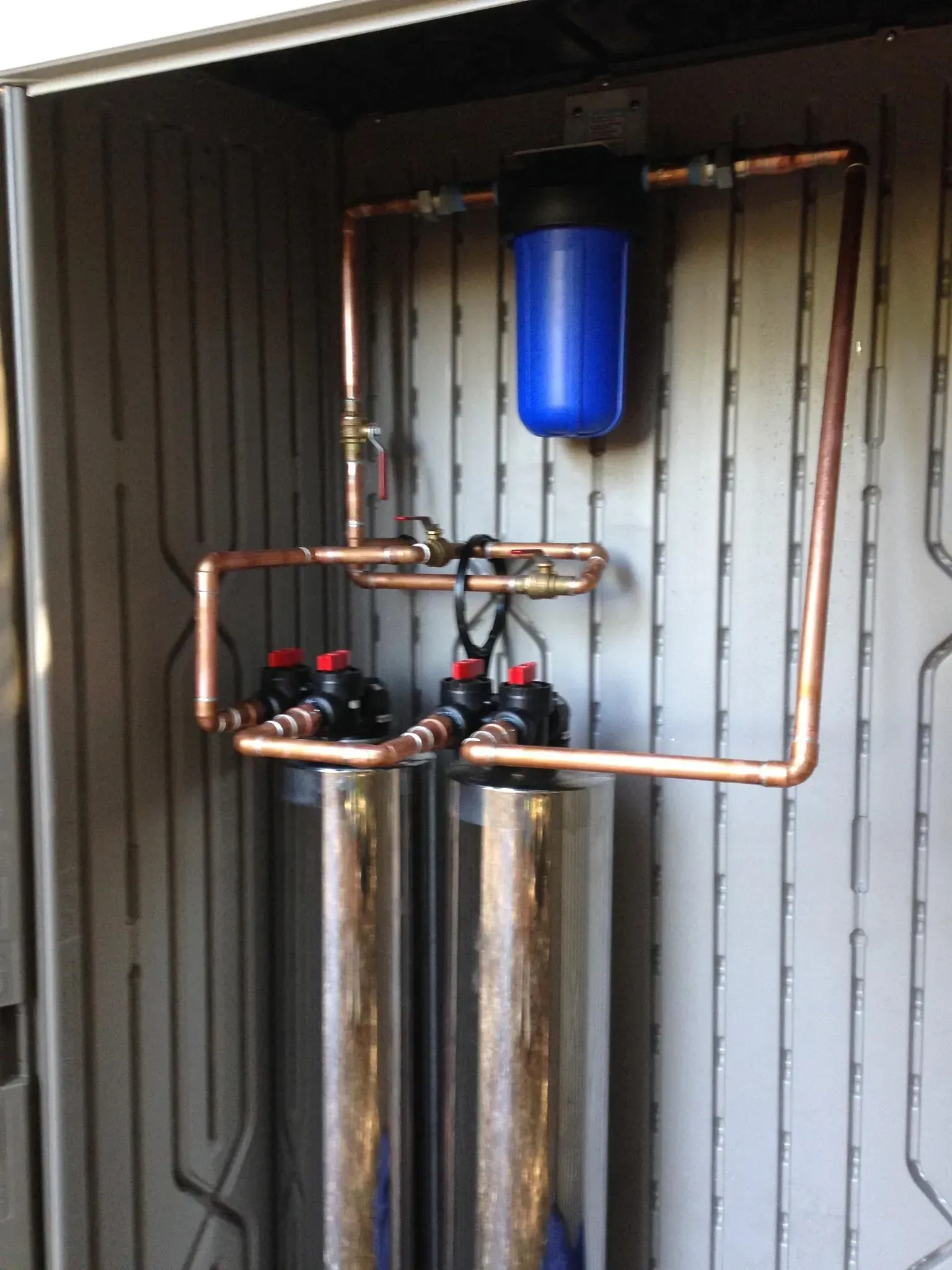 Copper piping and a blue tank in a utility closet, likely part of a water filtration system