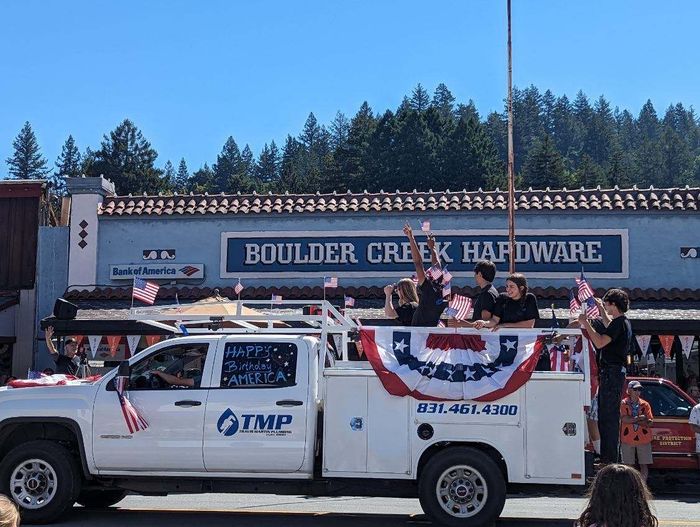 Decorated white utility truck in a parade in front of Boulder Creek Hardware storefront