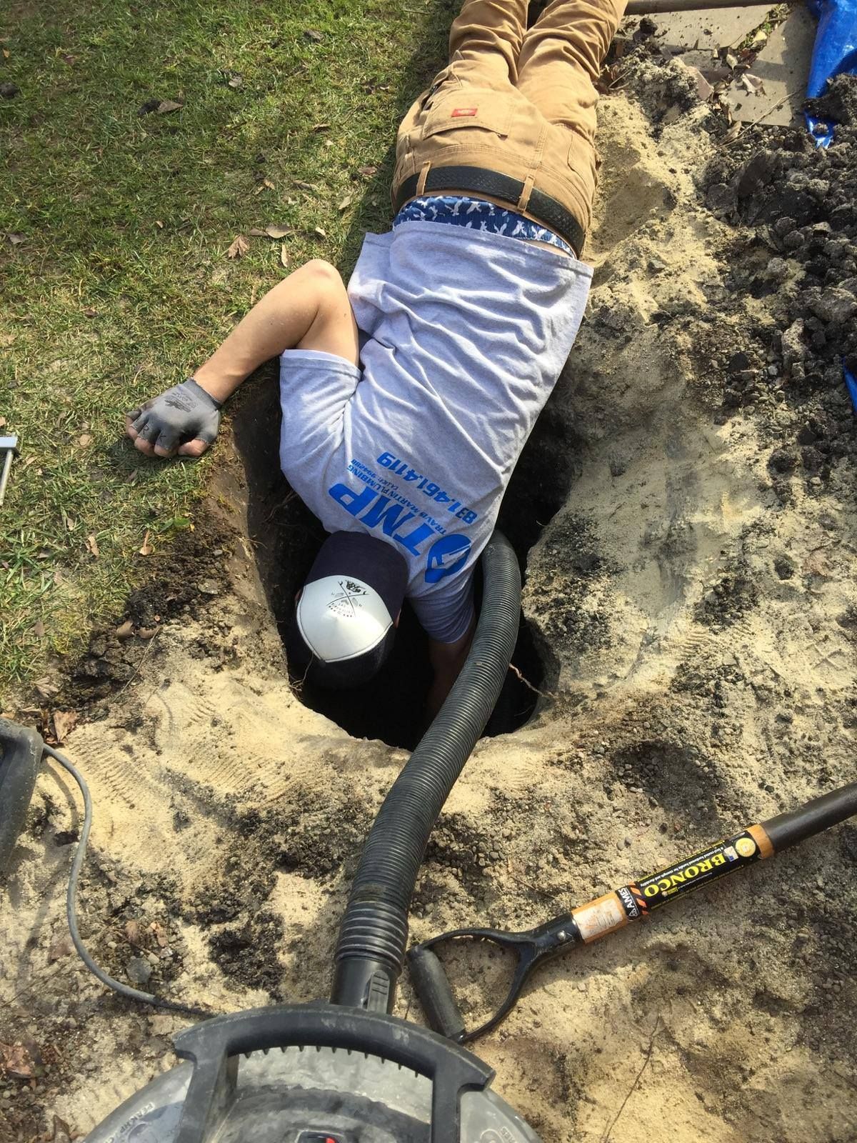 Worker in a dirt trench using a vacuum hose for excavation or cleanup