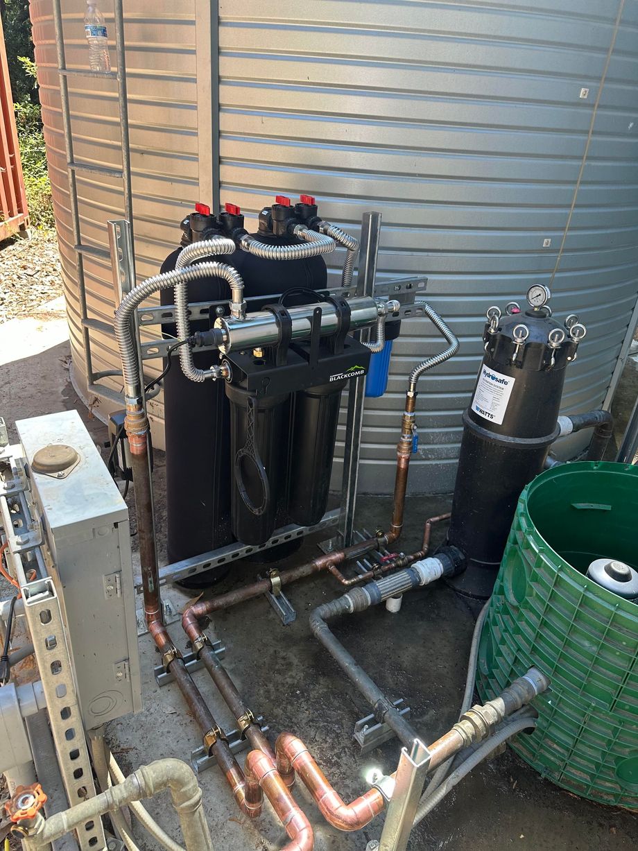 Outdoor industrial piping and black tanks beside a corrugated metal wall, with copper pipes on the ground.