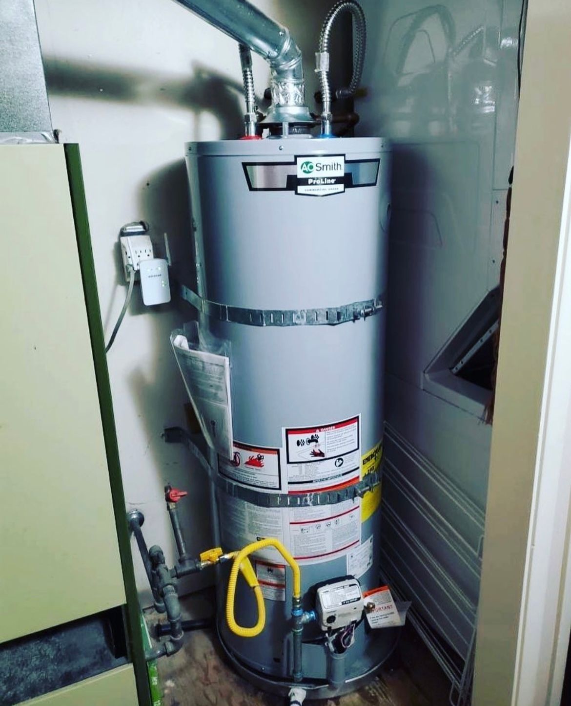 Tall gray water heater with pipes and labels in a narrow utility closet