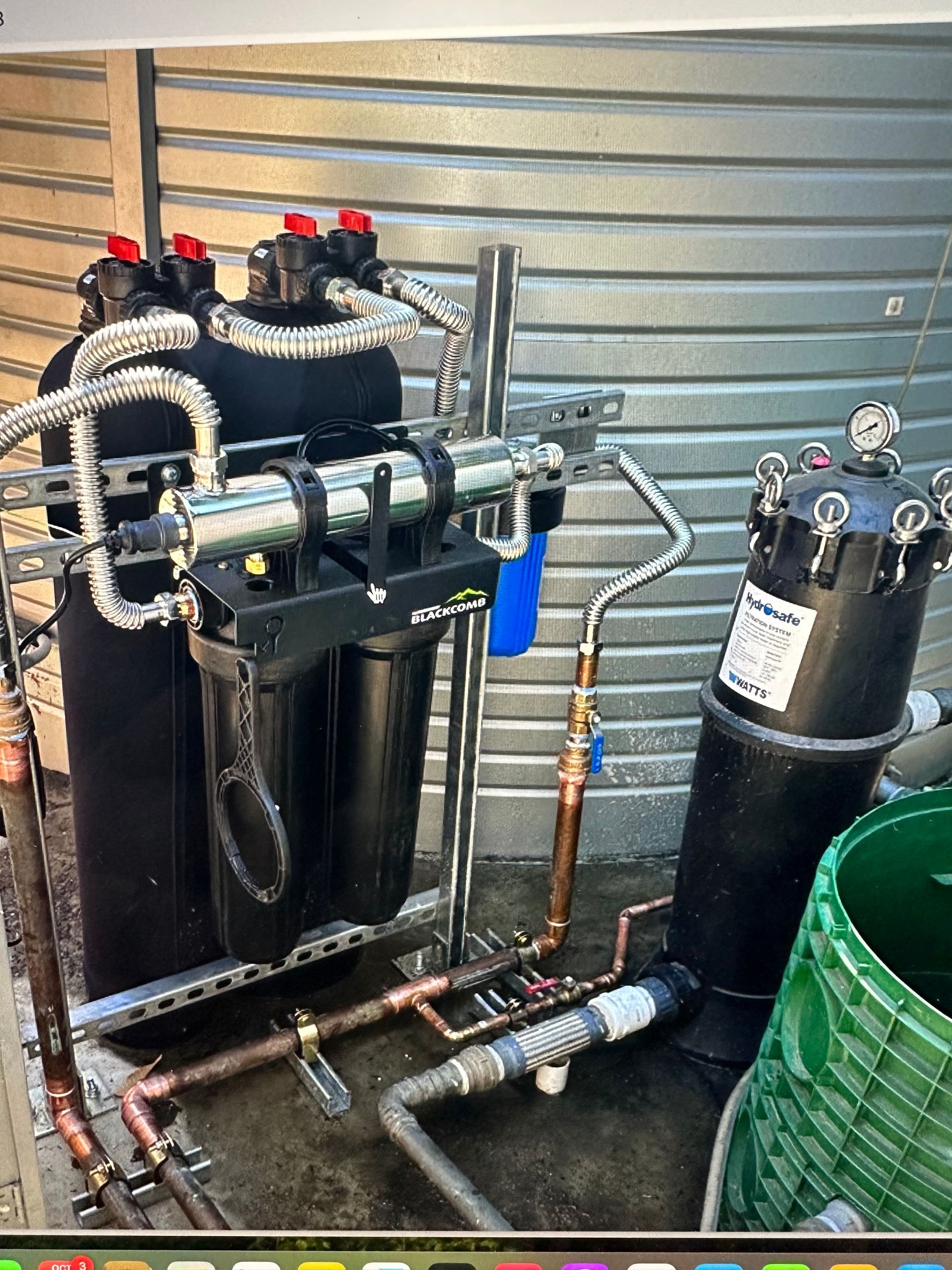 Industrial water filtration system with black tanks, pipes, valves, and a green container in a utility area