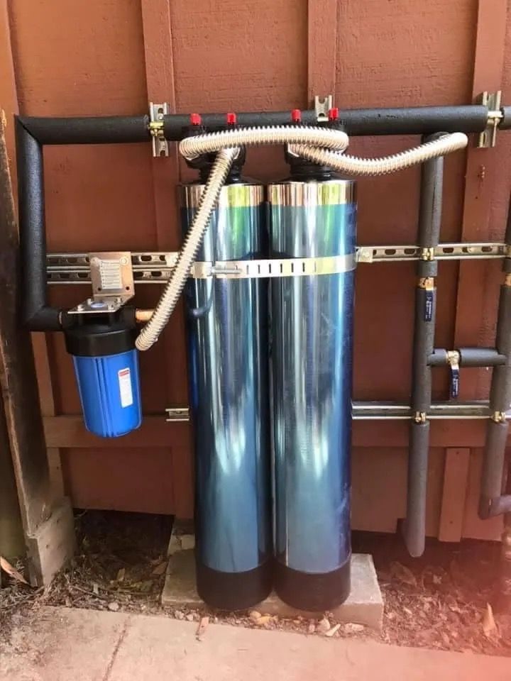 Two blue cylindrical water tanks and a blue filter on a wall-mounted plumbing setup outdoors
