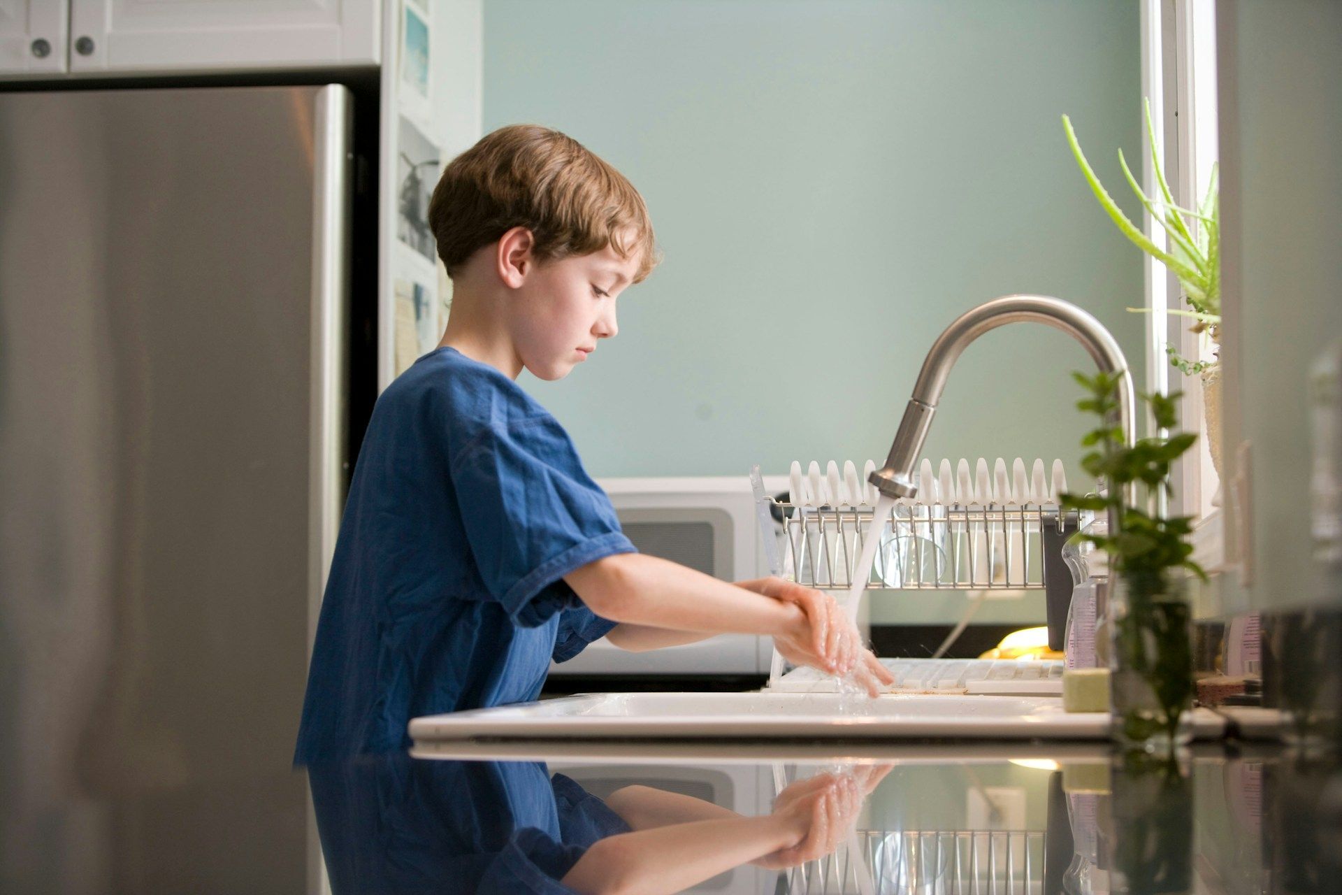 Boy washing dishes at a kitchen sink in a bright home kitchen