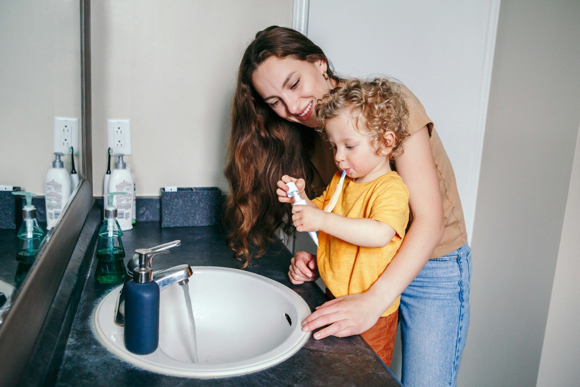 Woman helping a child wash hands at a bathroom sink