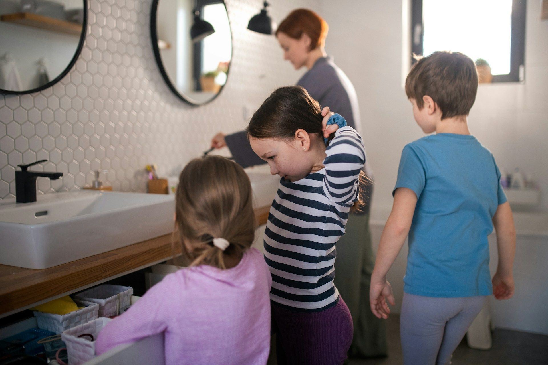 Children washing hands at a bathroom sink while an adult stands nearby