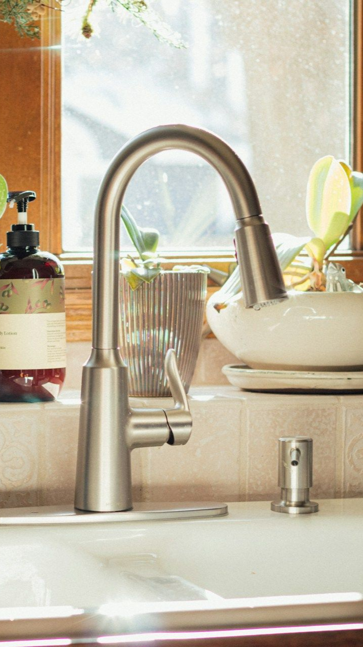 Kitchen sink with tall stainless faucet, soap dispenser, and dish by a bright window