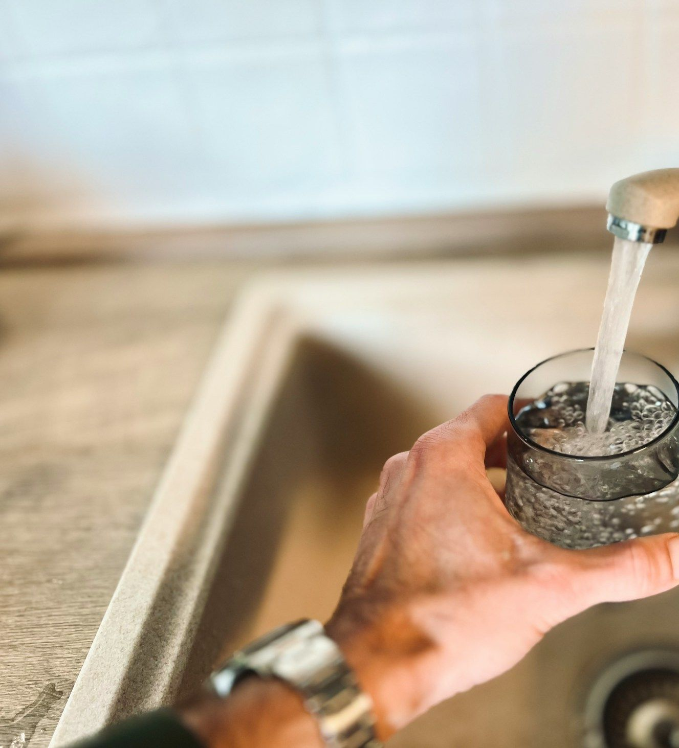 Hand filling a clear glass with running water at a kitchen sink