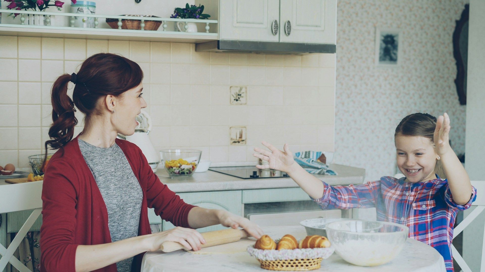 Woman and child in a kitchen, preparing food together at a table with bowls and a tray of baked goods