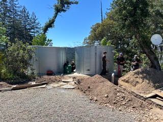 Outdoor yard with large metal tank, dirt piles, trees, and a few people working nearby