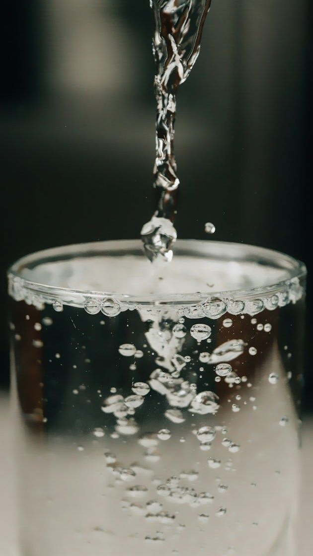 Water pouring into a clear glass, creating bubbles against a blurred dark background