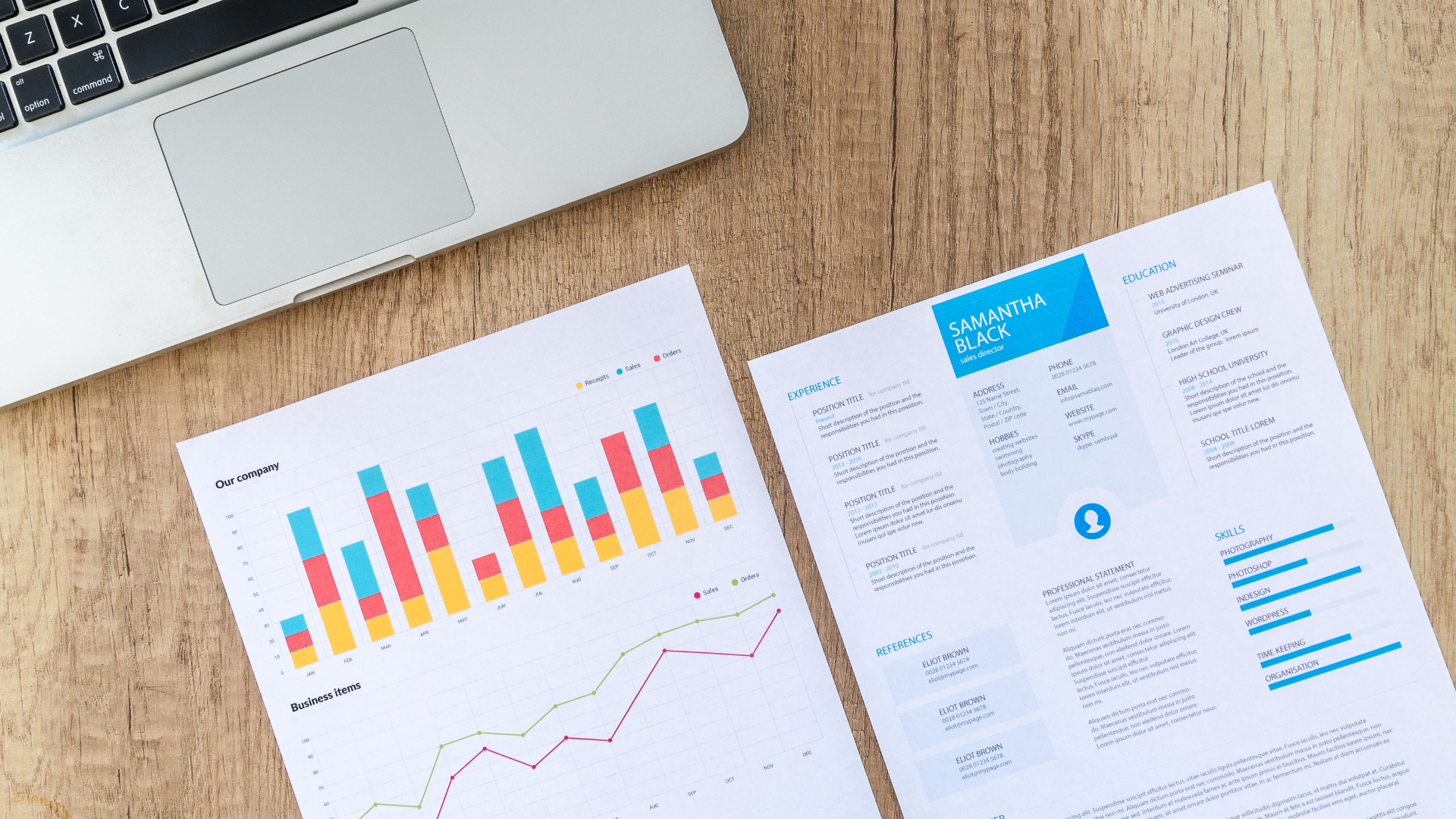 Laptop next to financial charts and documents on a wooden desk.