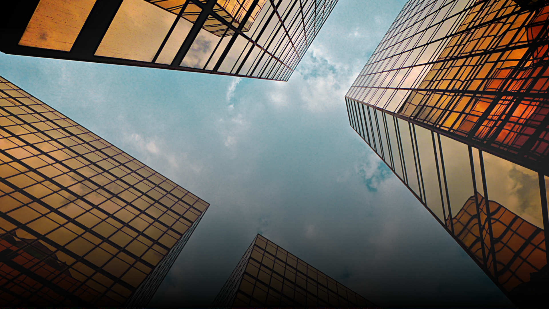 Skyscrapers with golden glass facades reaching toward a cloudy sky.