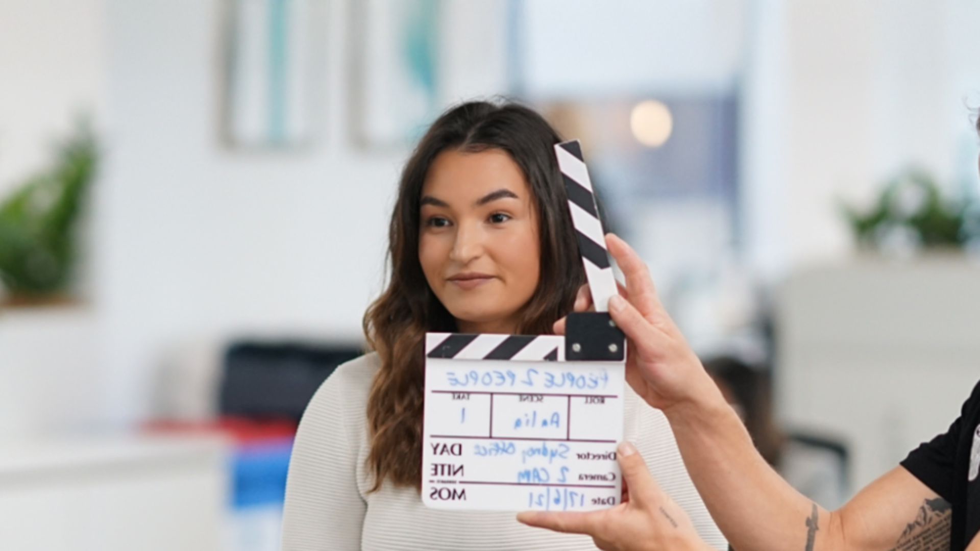 Woman on a set with a clapperboard. White clapperboard is in front of woman, held by a hand.