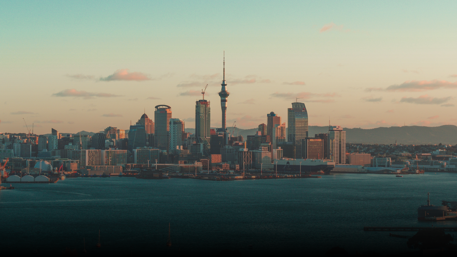City skyline at sunset, featuring the Sky Tower, overlooking harbor waters.