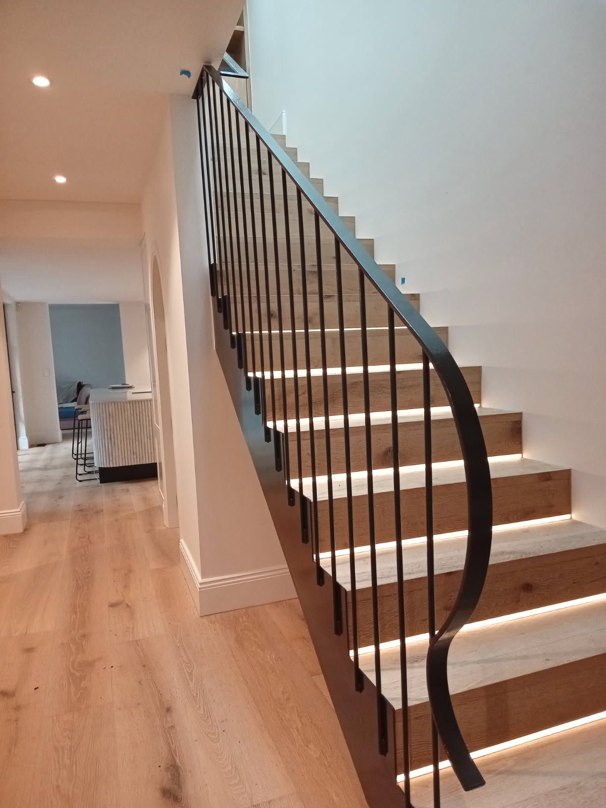 Modern staircase with black railing and illuminated wooden steps in a bright hallway — FBM Fabrication In Dapto, NSW