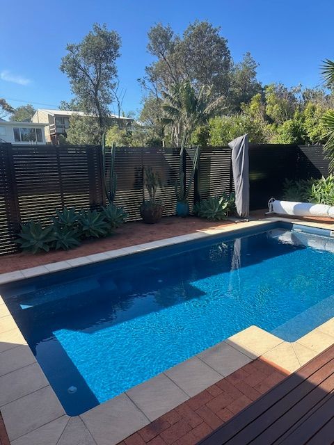 Backyard swimming pool with blue water, brick deck, and wooden privacy fence under sunny sky — FBM Fabrication In Dapto, NSW