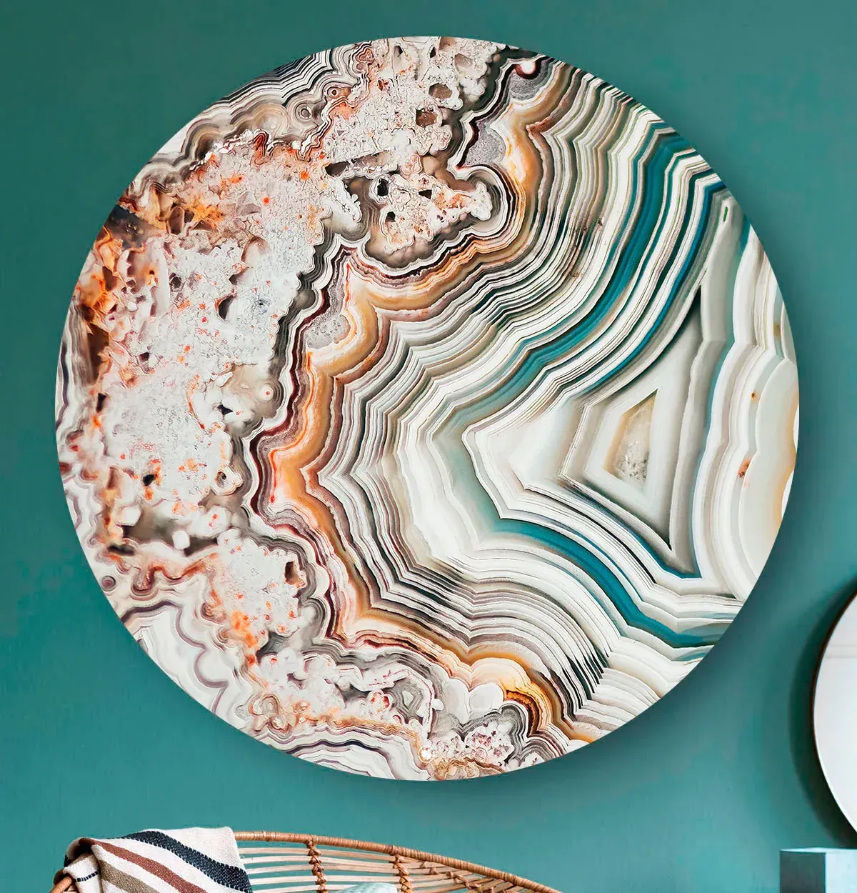 Rond abstract wandkunstwerk met gelaagde, agaatachtige banden in de kleuren turquoise, wit, oranje en grijs op een turquoise muur.