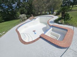 Backyard swimming pool with a curved brick edge, steps, and two people lounging in the sun
