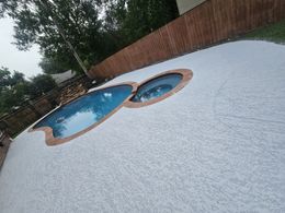 Backyard pool with a white pebble deck, blue water, and a brick fence around it