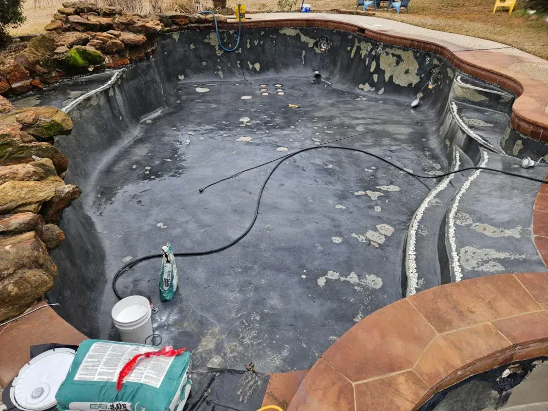 An empty, dark gray pool under renovation with a bucket and supplies on the bottom.