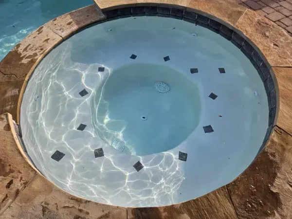A circular spa with light blue water and dark square decorative tiles inset along the seating area.