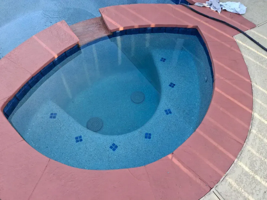 A crescent-shaped spa pool with blue water and decorative tile accents, surrounded by a reddish stone coping.