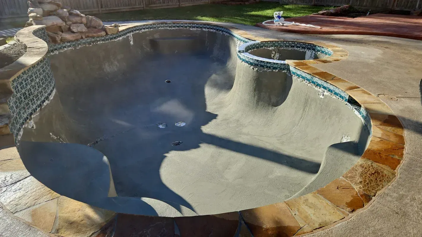An empty, freshly plastered swimming pool and spa surrounded by stone decking in a backyard setting.
