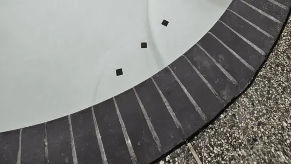A close-up view of a curved pool edge with dark grey tiles, contrasting with the smooth white interior of the pool.
