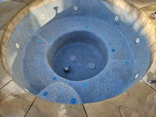 A round, empty hot tub with a blue speckled finish and integrated seating, set into a stone patio.