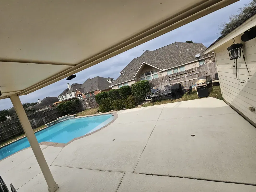 A covered patio overlooks a backyard swimming pool and neighboring houses on a cloudy day.