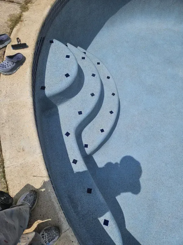 A high-angle view of gray pool steps with decorative black tile accents submerged in a light blue swimming pool.