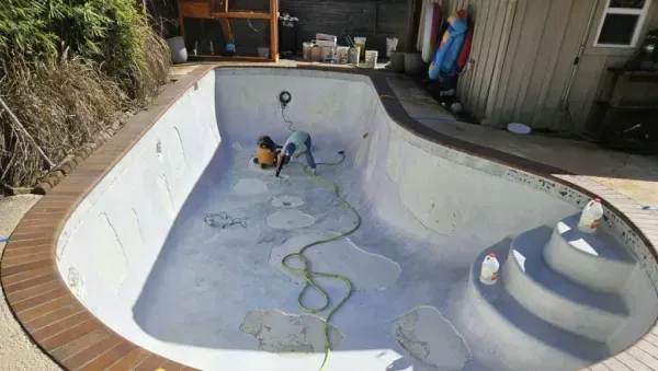 Two people work on a renovation inside an empty, light-colored swimming pool with curved steps.