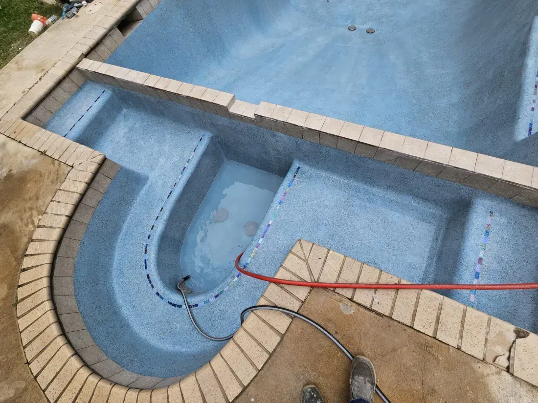 A partially filled, light blue tiled swimming pool with stone coping and stepped seating, viewed from above.