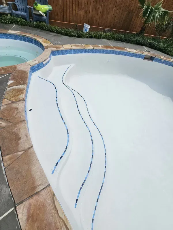An empty swimming pool with white interior, blue tiled steps, and a stone deck next to a separate hot tub.