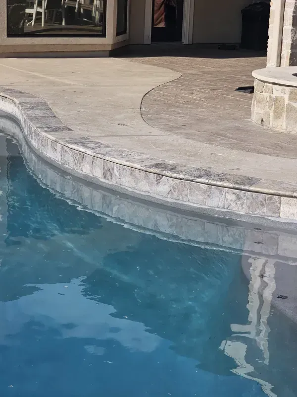 A swimming pool with a stone coping edge next to a concrete and paved patio area.