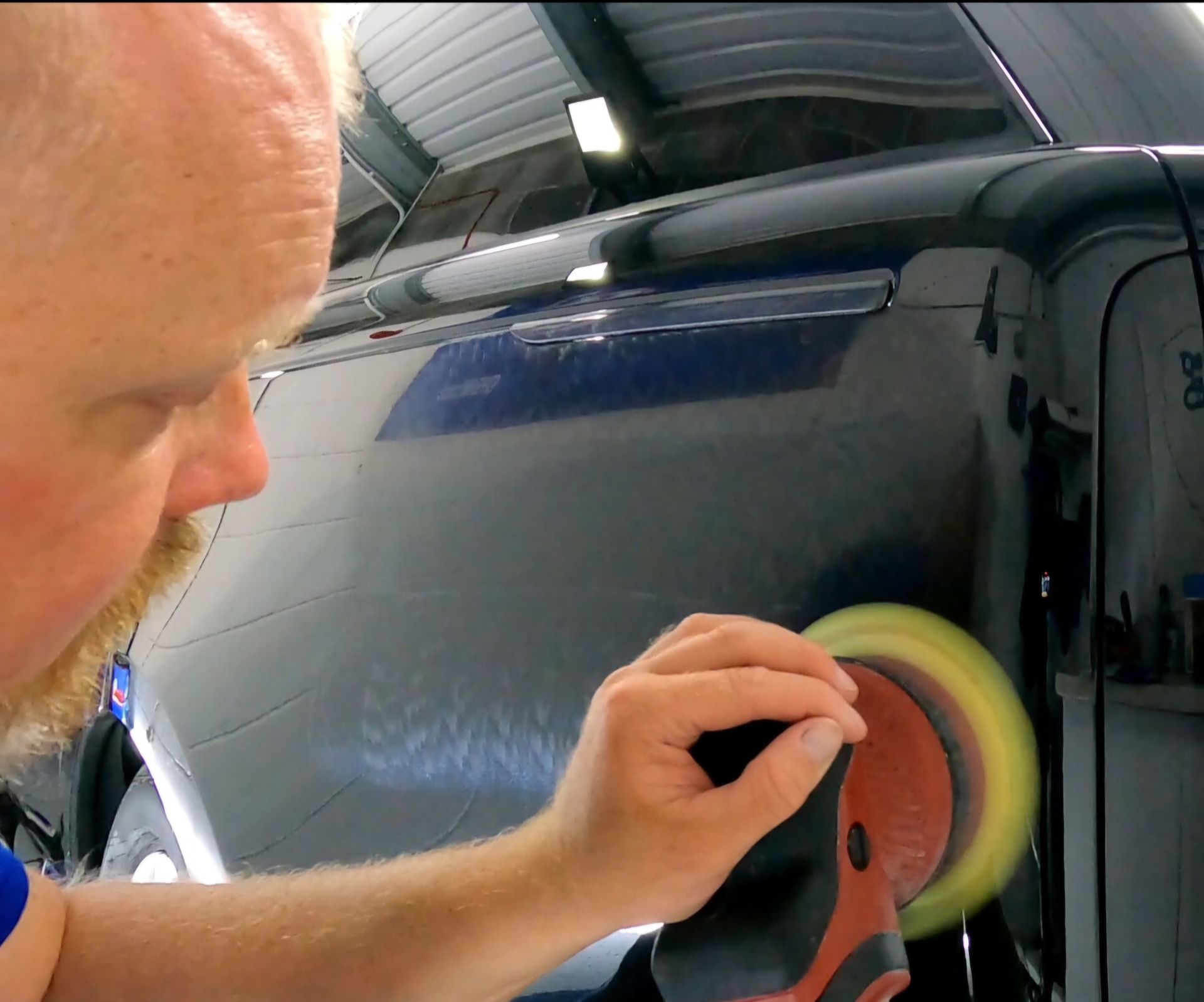 A man is polishing a car with a yellow polisher