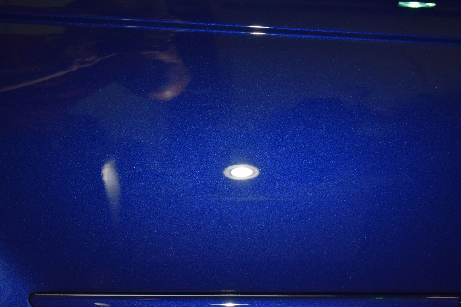 A close up of a blue car hood with a light reflected in it.
