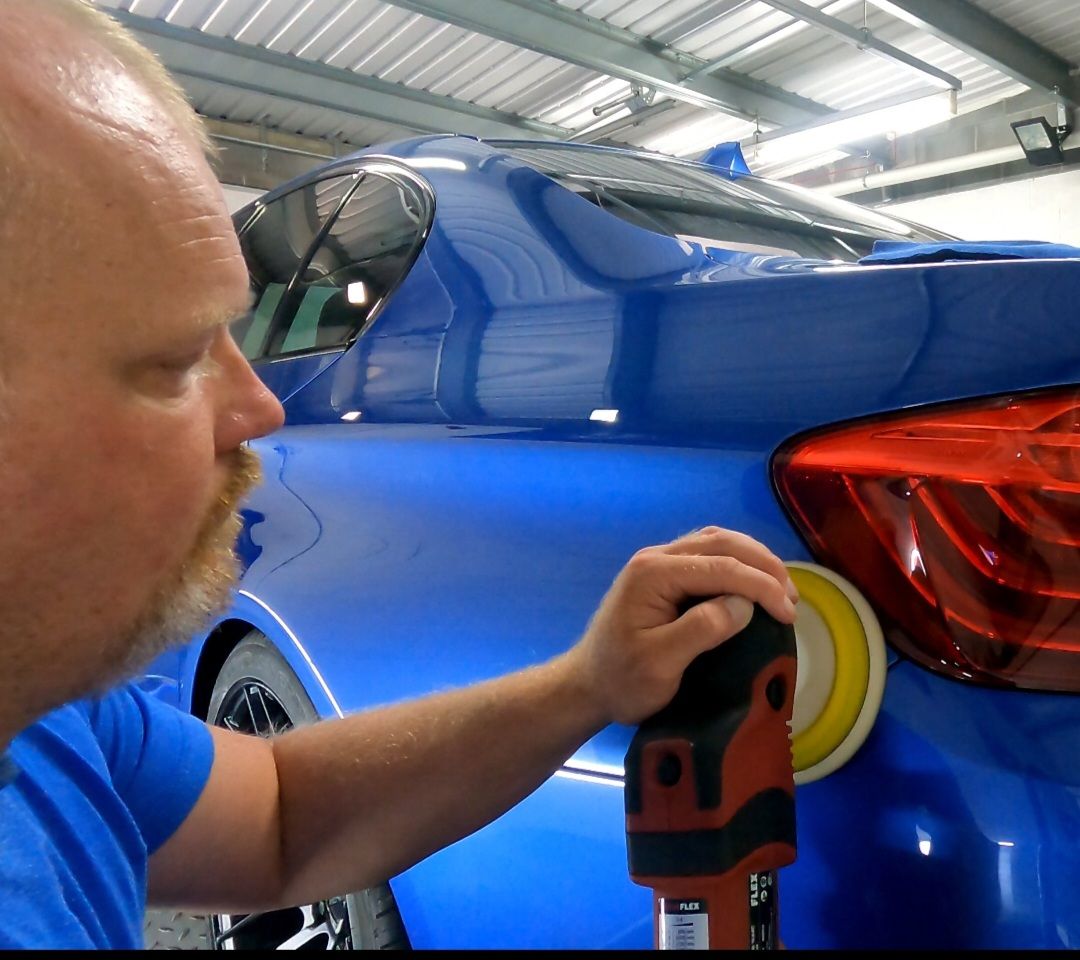 A man in a blue shirt is polishing a blue car