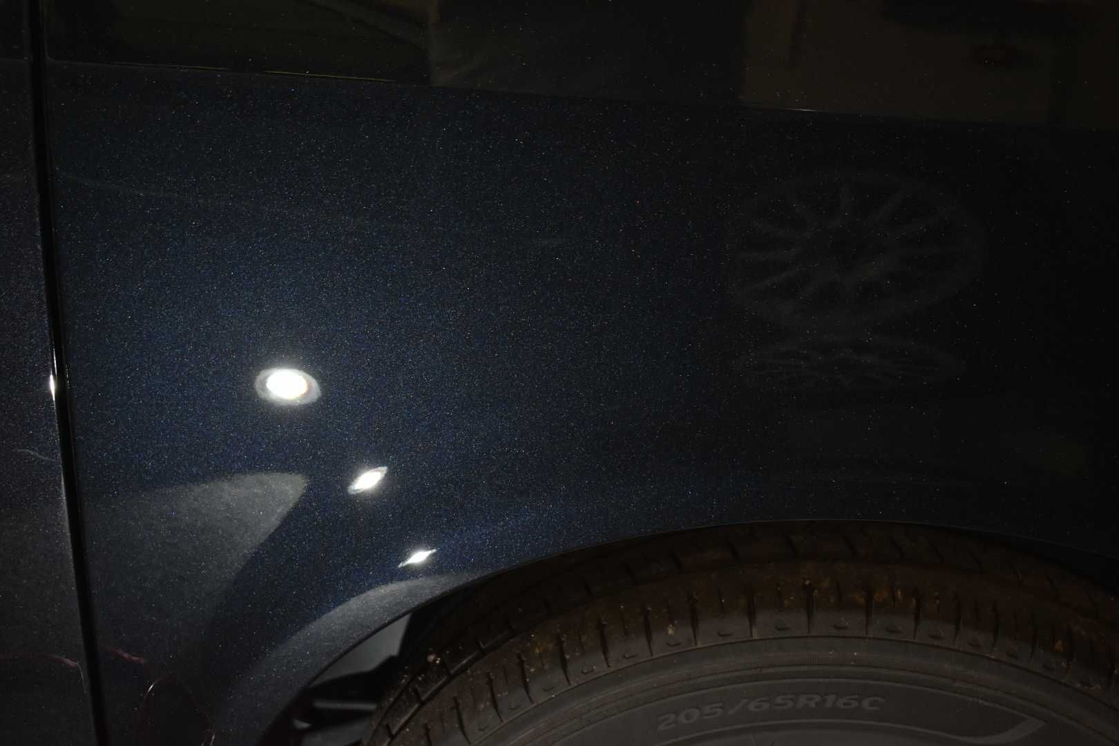 Dark blue car fender and wheel in low light with a bright reflection on the paint