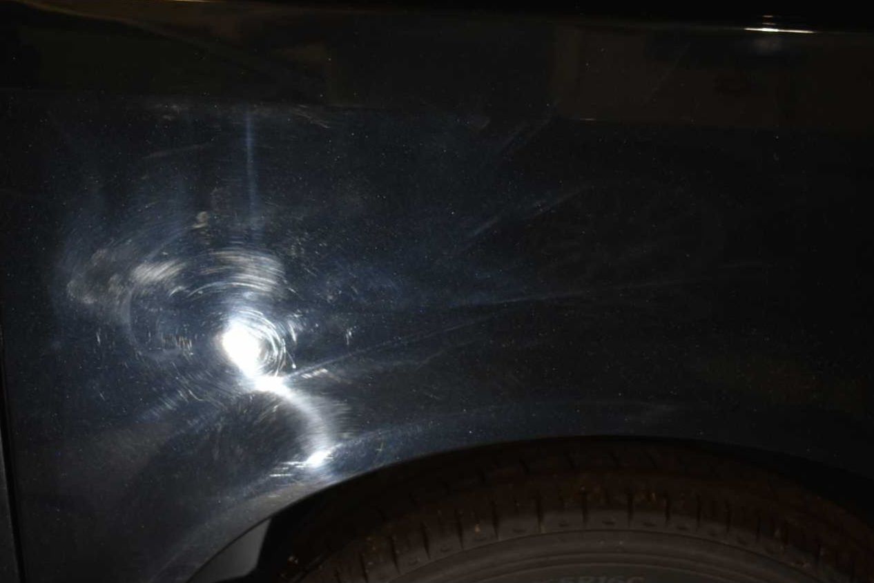 Close-up of a dark car fender with a bright dent and paint scratch near the wheel arch