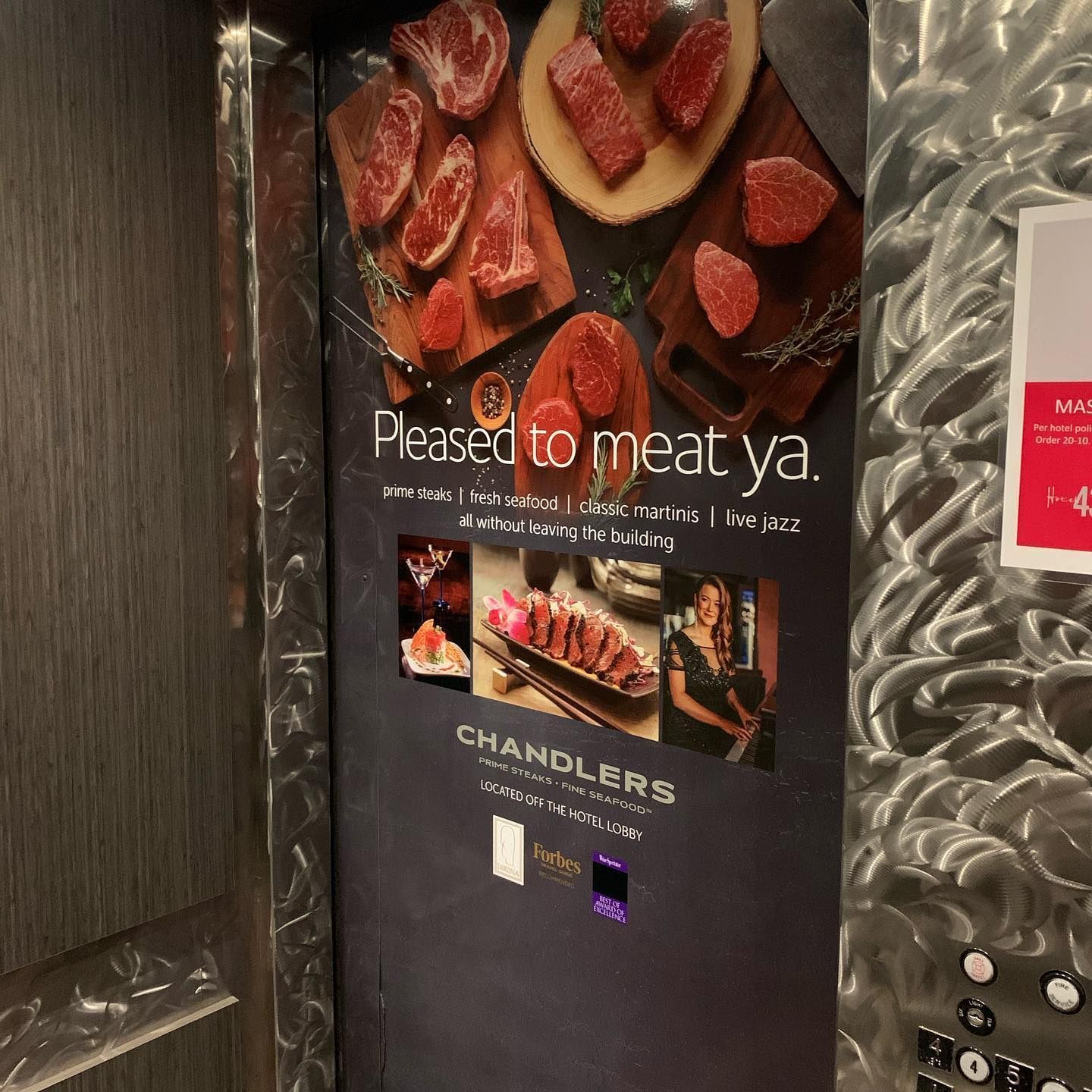 A promotional elevator sign for Chandlers Steakhouse featuring various cuts of raw and cooked meat, with text and logo.