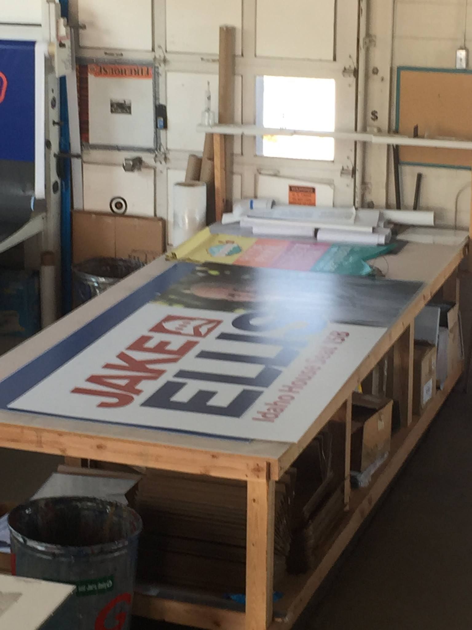 A large political campaign sign for Jake Ellis on a wooden workbench inside a print shop.