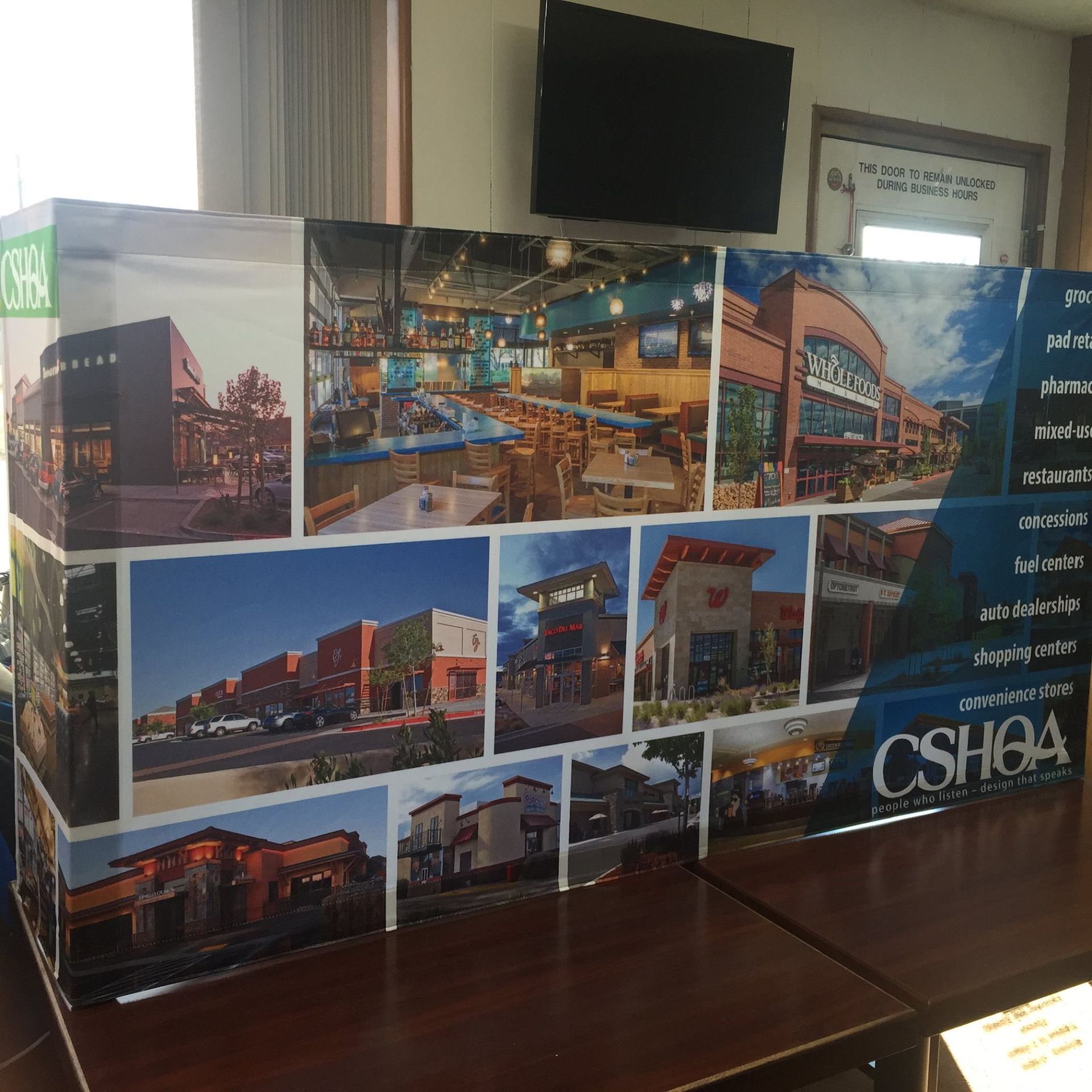 A CSHOA display board showing a collage of architectural and interior images of commercial buildings on a wooden table.